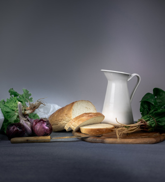 still life. jug, bread, onion, garlic, spinach on a blue tablecloth. space for text - 写真・画像