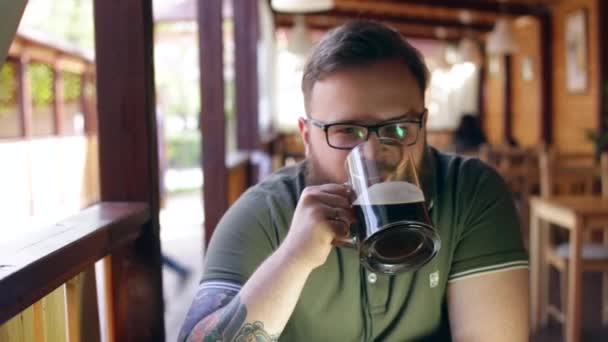 Tattooed, bearded man sitting at the bar on the summer porch - Imágenes, Vídeo