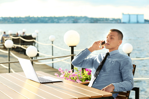 Geschäftsmann arbeitet am Laptop und telefoniert im Freien - Foto, Bild