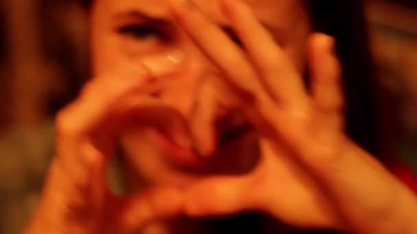 Κορίτσι δείχνει μια καρδιά σε ένα χρώμα φόντου και χαρακτηριστικά αστεία πρόσωπα - Πλάνα, βίντεο