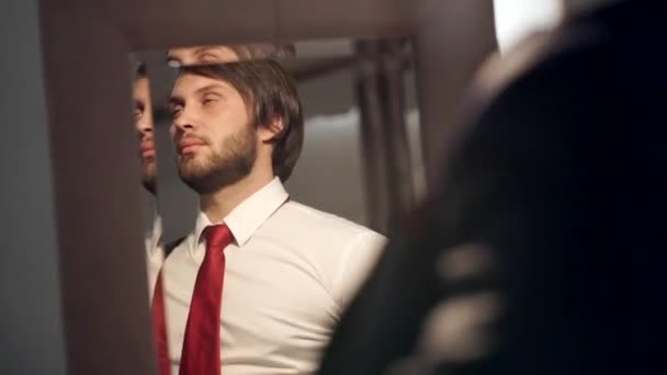 Brutal bearded man dressed in a beautiful wedding day. The groom wears a red tie in the reflection of a mirror coat - Záběry, video
