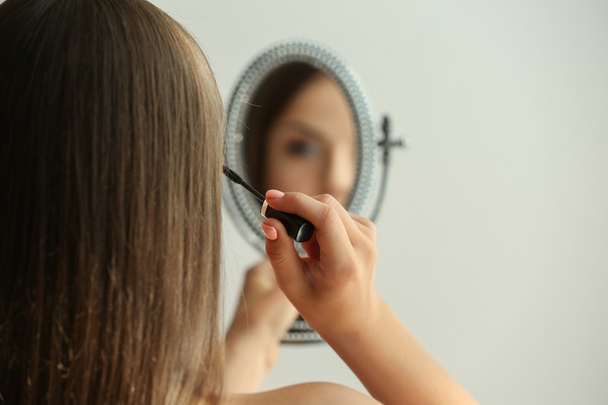 Beautiful young woman looking in mirror while applying makeup - Fotoğraf, Görsel