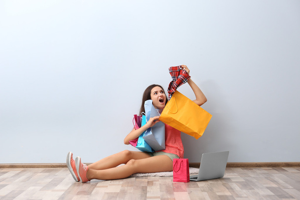 Щаслива молода жінка з барвистими сумками для покупок і ноутбуком, що сидить на підлозі
 - Фото, зображення
