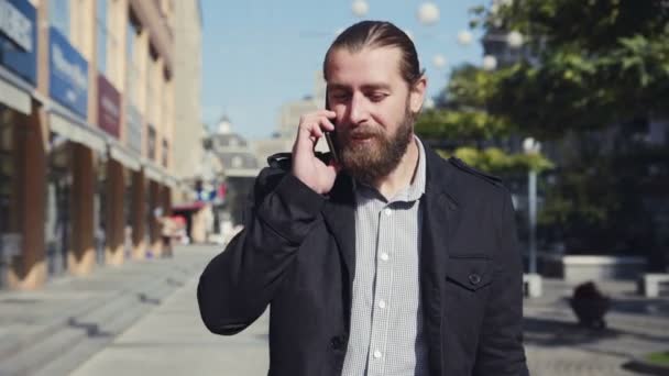 Hombre barbudo caminando por la calle de la ciudad y hablando por teléfono
 - Metraje, vídeo