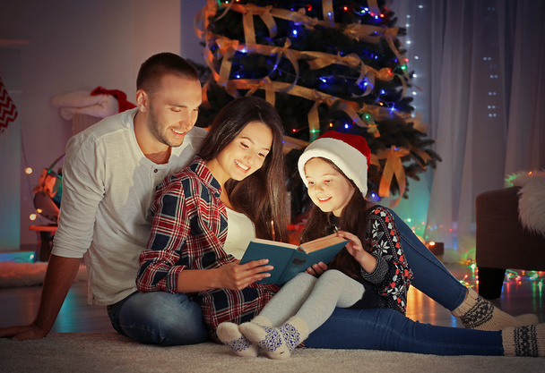 Little girl and her family reading book in living room decorated for Christmas - Photo, Image