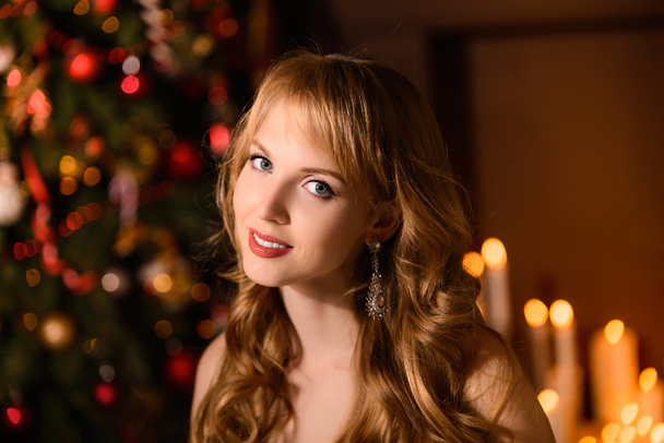 Young beautiful blond woman in the white dress on christmas, woman in a beautiful room with a Christmas tree and candles, a girl with gifts,  golden hair, happy woman new year, Redhead girl smiling  - Photo, image