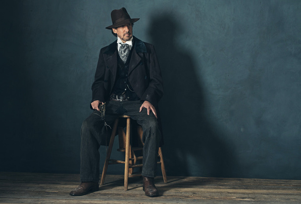 Zralý muž s revolverem sedí na stoličce - Fotografie, Obrázek