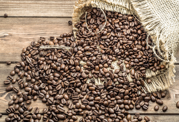 Black coffee beans in burlap sack on wooden table - Фото, зображення