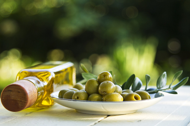 dish of olives and oil bottles on green background - Fotoğraf, Görsel