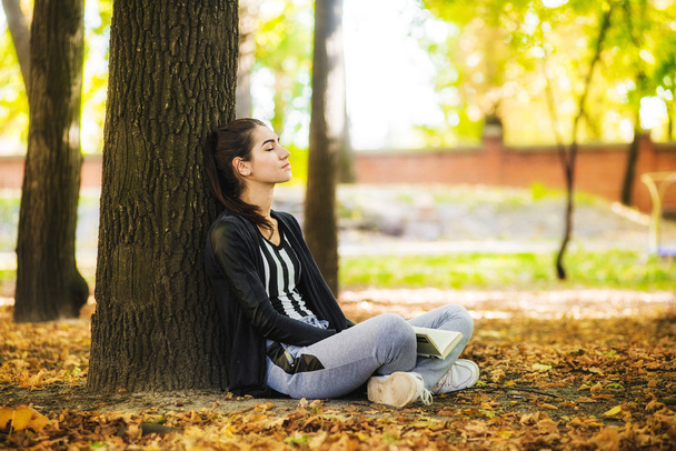 La chica con el libro sentado debajo del árbol
 - Foto, imagen