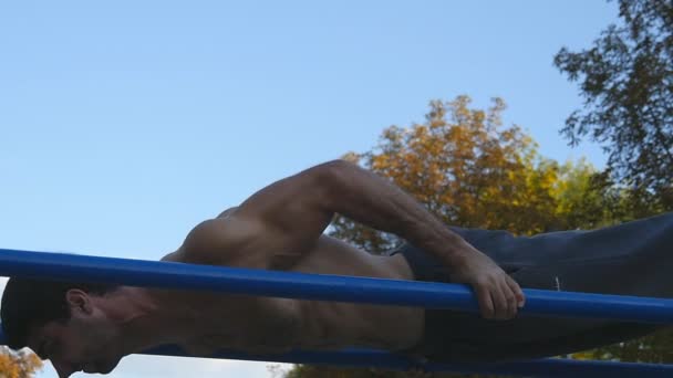 Athletic man doing push ups on parallel bars at sports ground in city park. Strong young muscular guy training outdoor in summer. Athlete exercising at playground. Slow motion. Closeup - Footage, Video