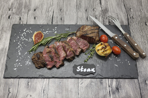 gegrilltes Striploin Steak auf einem Steinteller mit Gabel und Messer. - Foto, Bild