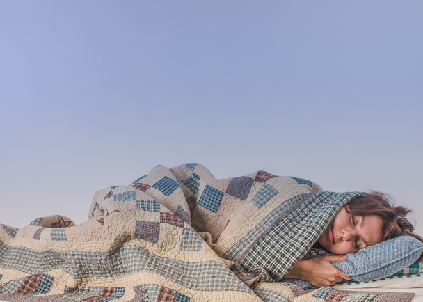 市松模様の毛布の下で寝ている若い女性 - 写真・画像