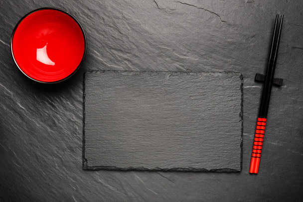 Две палочки для еды и красная табличка на фоне черного камня с копирайтом, вид сверху
 - Фото, изображение