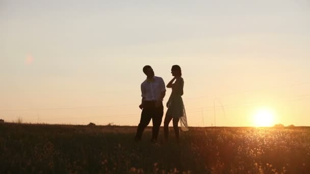 Young couple silhouettes dancing on the field at sunset - Materiał filmowy, wideo