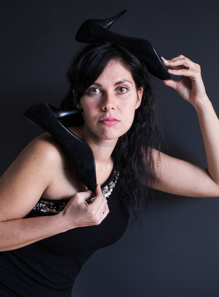 grappige foto portret van dark haired model in zwarte jurk over haar schouder met tuflemi hoge hakken op haar hoofd - Foto, afbeelding
