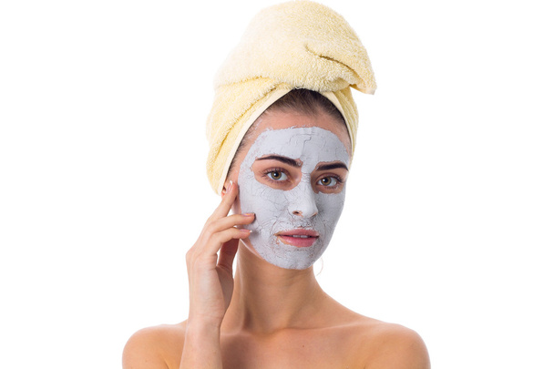 Vrouw met handdoek op haar hoofd en cosmetische masker op haar gezicht - Foto, afbeelding