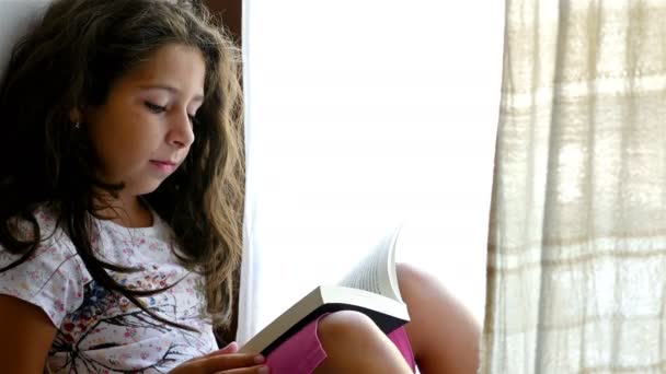 Χαριτωμένο μικρό κορίτσι που κάθεται στο περβάζι ενός παλιού σπιτιού, διαβάζοντας το βιβλίο για το παιχνίδι της αρκούδας - Πλάνα, βίντεο