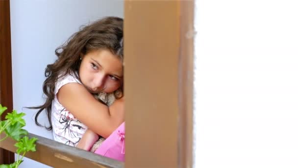 Kétségbeesett magányos kislány ült az ablaknál egy régi ház neki medve játék, dolly - Felvétel, videó