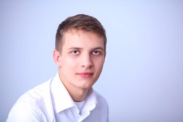 Portrait of young man smiling sitting on gray background - Fotografie, Obrázek