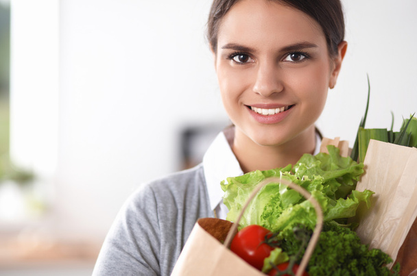 Young woman holding grocery shopping bag with vegetables . Standing in the kitchen - Foto, Bild