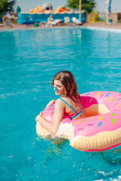 Young girl in sprinkled donut float at pool - Foto, Bild