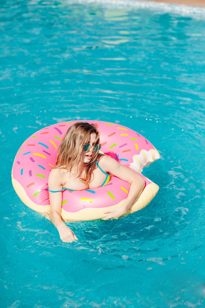 Young girl in sprinkled donut float at pool - 写真・画像
