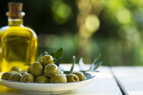 dish of olives and oil bottles on green background - Foto, afbeelding