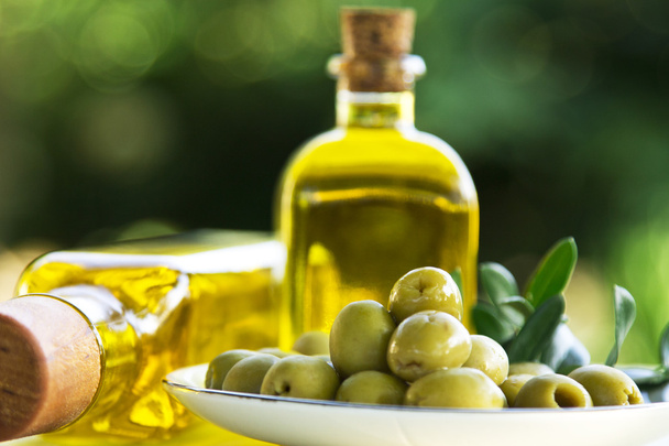 dish of olives and oil bottles on green background - Photo, Image