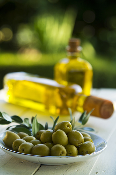 dish of olives and oil bottles on green background - Foto, Imagen