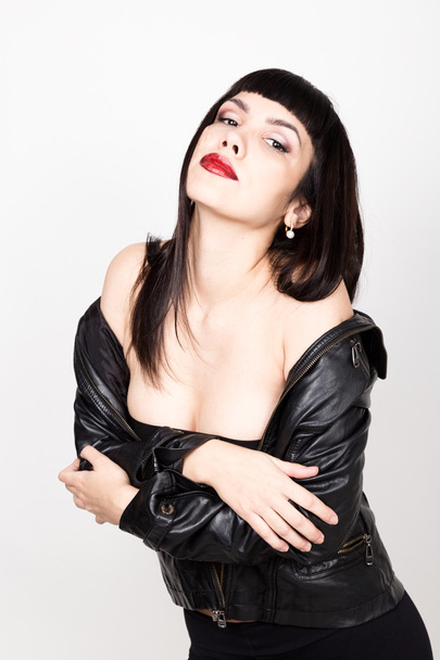 Portrait of beautiful young woman in a leather jacket, standing turned with bare shoulders. posing at camera - Foto, immagini