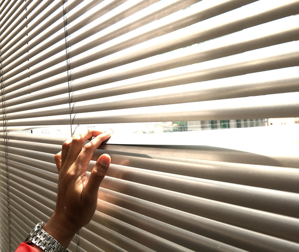 Hand nemen van een kijkje via de venster blinds - Foto, afbeelding