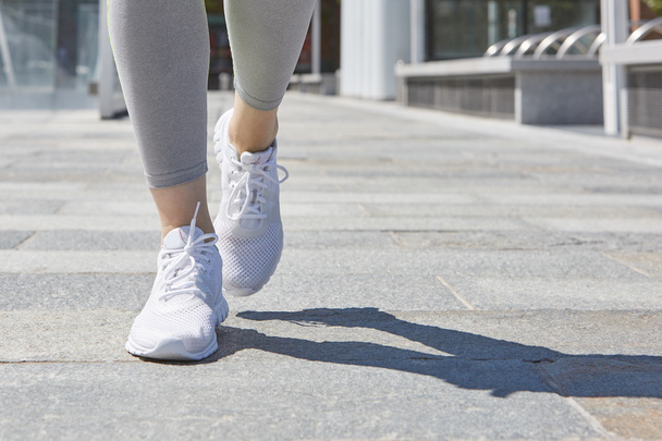 Woman running in a sunny city, close up on shoes - Foto, Bild