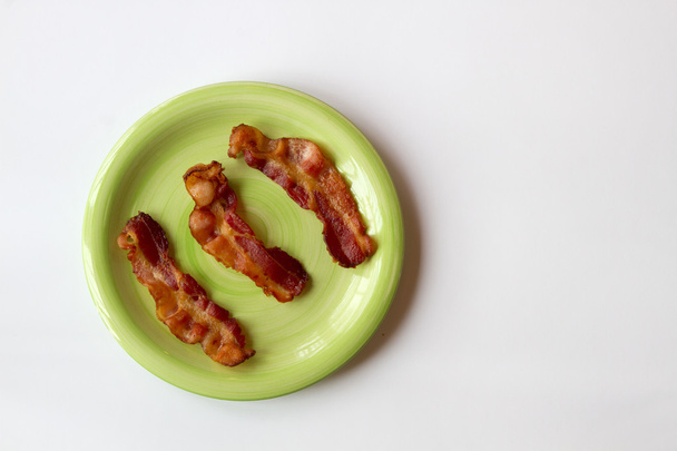 Trois morceaux de bacon sur une plaque verte isolés sur un dos blanc
 - Photo, image