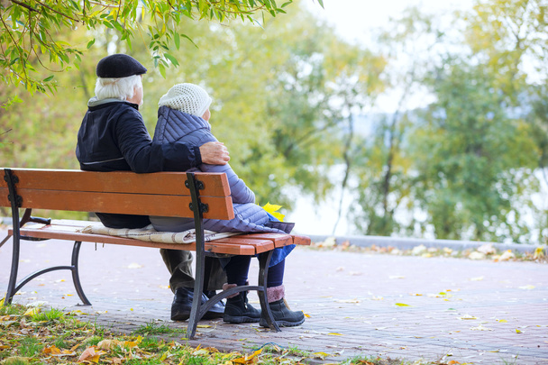 Старшая пара сидит на скамейке в осеннем парке
  - Фото, изображение