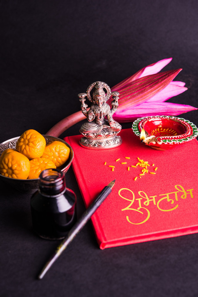 Une écriture indienne de bon augure Shubha Labh signifie "Bonté" & "Richesse", sur le livre de notes comptables rouge / "bahi khata" avec la déesse Laxmi, diya, bonbons et lotus et stylo à l'encre sur laxmi pujan, sur diwali
 - Photo, image