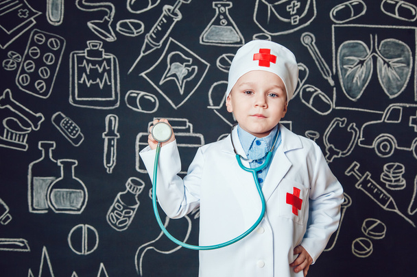 Happy little boy as a doctor holding sthetoscope on dark background with pattern - Photo, image