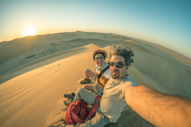 ナミブ砂漠、ナミブ国立ウクルフトパの砂丘地の主な selfie を取る大人のカップル旅行、ナミビア、アフリカの先です。バックライト、引き締まったイメージの魚眼ビュー. - 写真・画像