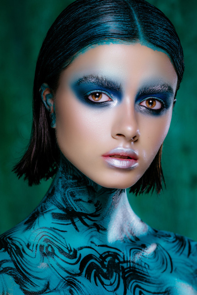 Art make-up in bright colors. Beautiful brunette girl in short hair posing in the studio on a turquoise background. Radiant skin - Fotografie, Obrázek