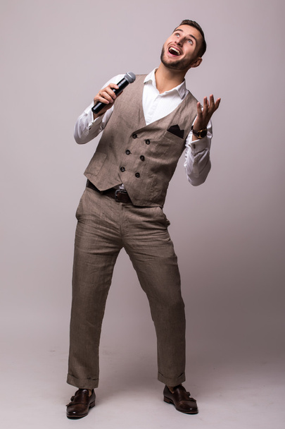 Νεαρός άνδρας στο κοστούμι τραγουδώντας πάνω από το μικρόφωνο με ενέργεια. - Φωτογραφία, εικόνα