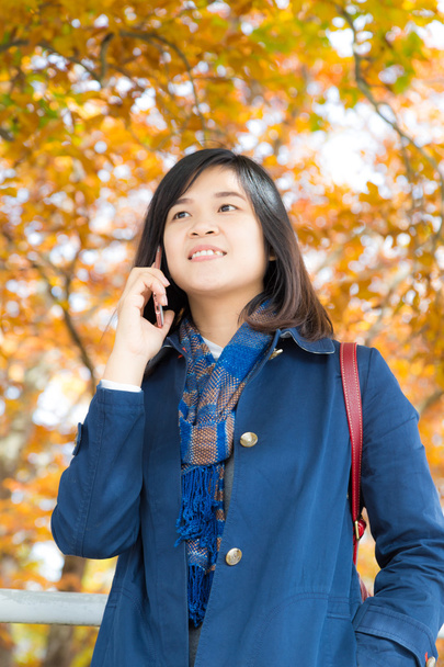 秋の公園で携帯電話スタンドに話幸せな若い女 - 写真・画像