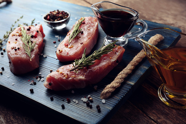 Raw steaks with herb and spices on wooden cutting board - Фото, изображение