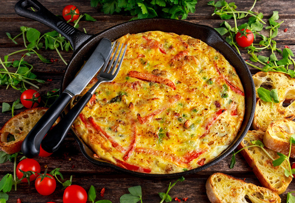 Frittata made of eggs, potato, bacon, paprika, parsley, green peas, onion, cheese in iron pan. on wooden table. - Photo, Image