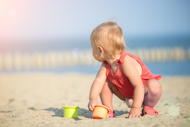 Baby girl in red dress playing on sandy beach near the sea. - Photo, Image