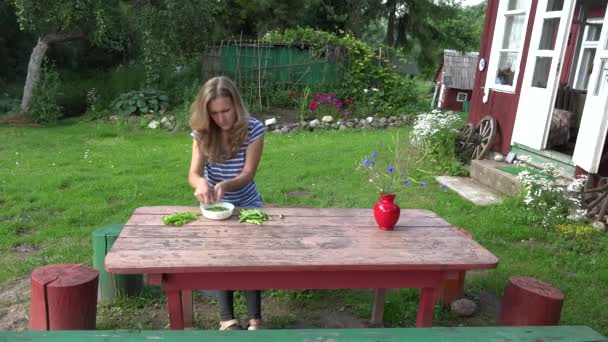 Dorpsbewoner blond meisje pod groene erwten op houten tafel in de buurt van vakantiehuis. 4k - Video