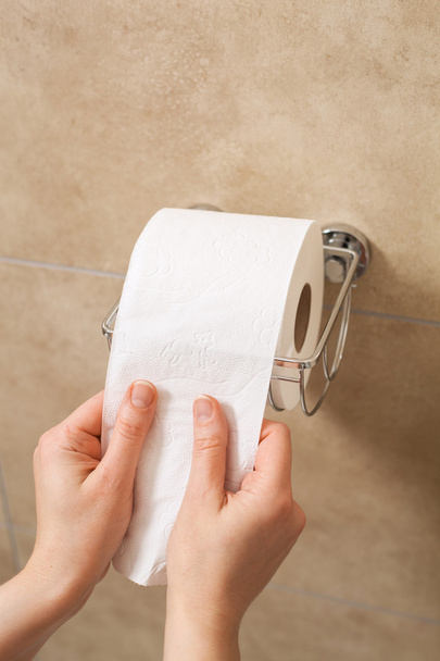 Hand zieht Toilettenpapierrolle in Halter - Foto, Bild