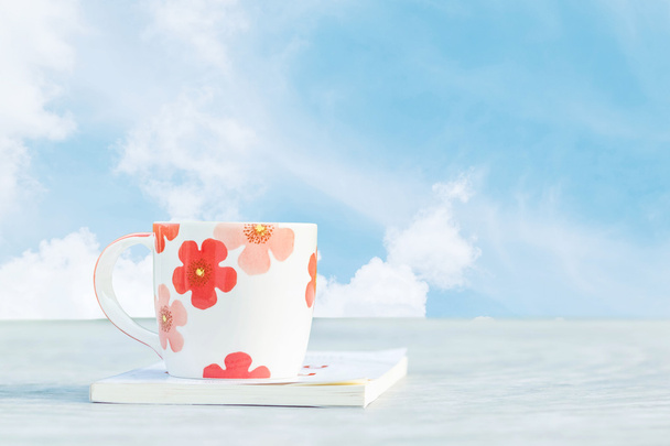 クローズ アップ コーヒー雲朝テクスチャ背景の美しい青い空と庭でぼやけコンクリート机の上の本は白のかわいいカップ - 写真・画像