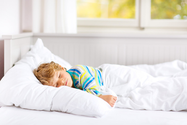 безтурботний маленький хлопчик спить у ліжку в барвистому нічному одязі
. - Фото, зображення