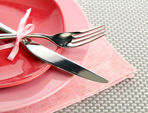 Vaaleanpunaiset tyhjät lautaset haarukalla ja veitsellä harmaalla pöytäliinalla
 - Valokuva, kuva