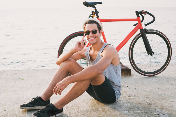 A rögzített hálót kerékpár beszél telefonon, a tenger közelében csípő fiatal férfi - Fotó, kép